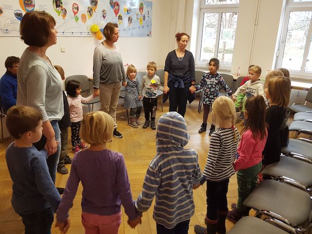 Foto von Kindern und drei Erziehern, wie sich im Kreis an den Händen halten.