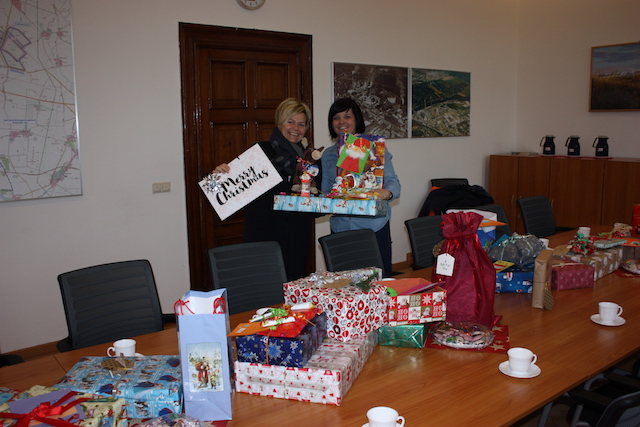Foto von einem Tisch mit Weihnachtsgeschenken, zwei Frauen stehe im Hintergrund.