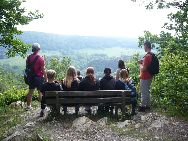 Foto von Jugendlichen auf einer Bank im Wald.
